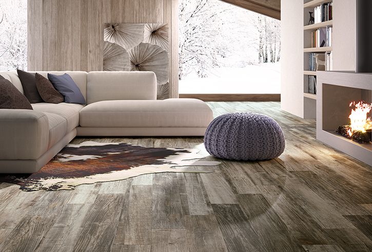 Shows a catalog scene featuring a wood look plank tile on the floor of a living room. It has contrasting mid and light tones, adding a lot of texture to the room.