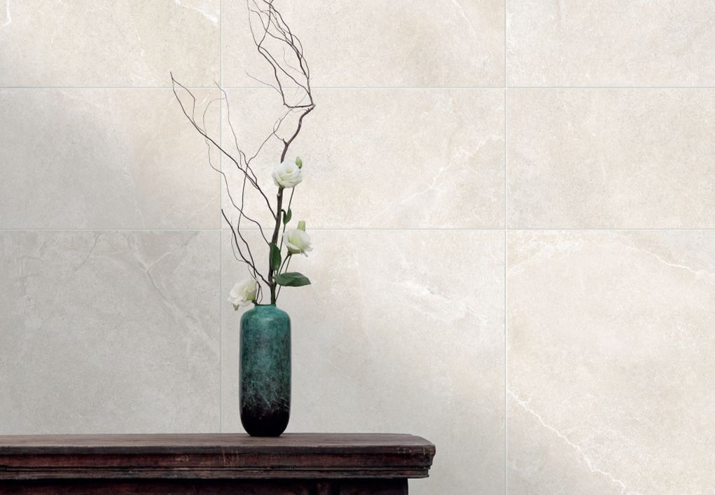 Shows a catalog scene featuring a creamy beige marble tile behind a modern looking flower pot with a small flower